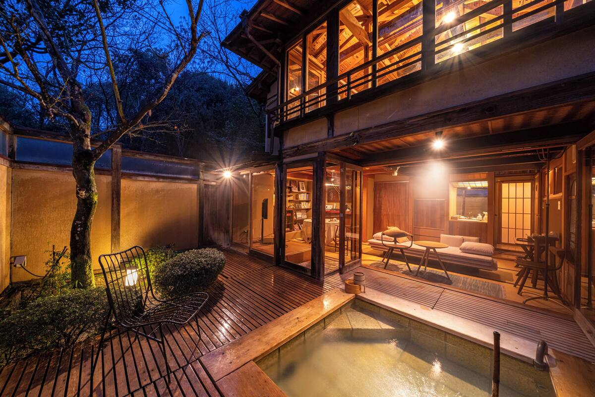 A traditional Japanese-style building with a wooden deck, a small pond, and a seating area with cushions and a low table.