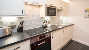 A modern kitchen with white cabinets, a microwave, a kettle, and a toaster. - 2 bedroom home within walking distance of the town - Pass the Keys (Shrewsbury)