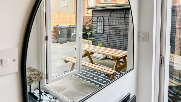 A view through a door into a courtyard with a wooden bench and a small garden. - Chic Beamish Retreat | Stylish 3-Bed Near Durham - Pass the Keys (Stanley)