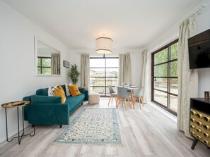 A modern living room with a teal sofa, a small round table, and a TV on a black stand.