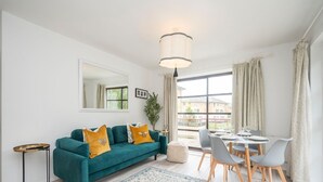 A modern living room with a teal sofa, a dining table with chairs, a large window with curtains, and a hanging light fixture. - London apartment - Waterfront Terrace & Parking - Pass the Keys (London)