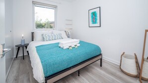 A modern bedroom with a bed, a window, a bedside table, a wall-mounted shelf, and a woven basket. - London apartment - Waterfront Terrace & Parking - Pass the Keys (London)
