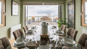 Een eetgedeelte met uitzicht op zee, een houten terras en een gedekte tafel voor zes personen.