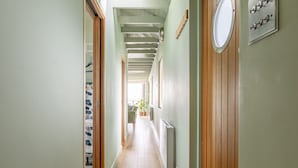 Een smalle gang met houten vloer, een radiator en een klok aan de muur.