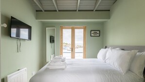 Een slaapkamer met een bed, een televisie, een radiator en uitzicht op zee door een deur.