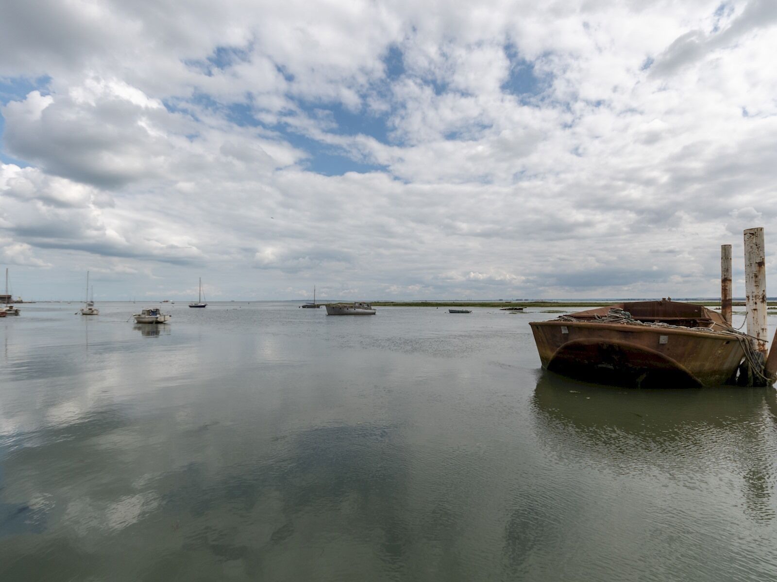A calm harbor with several boats, including a rusted boat in the foreground and a sailboat in the distance.