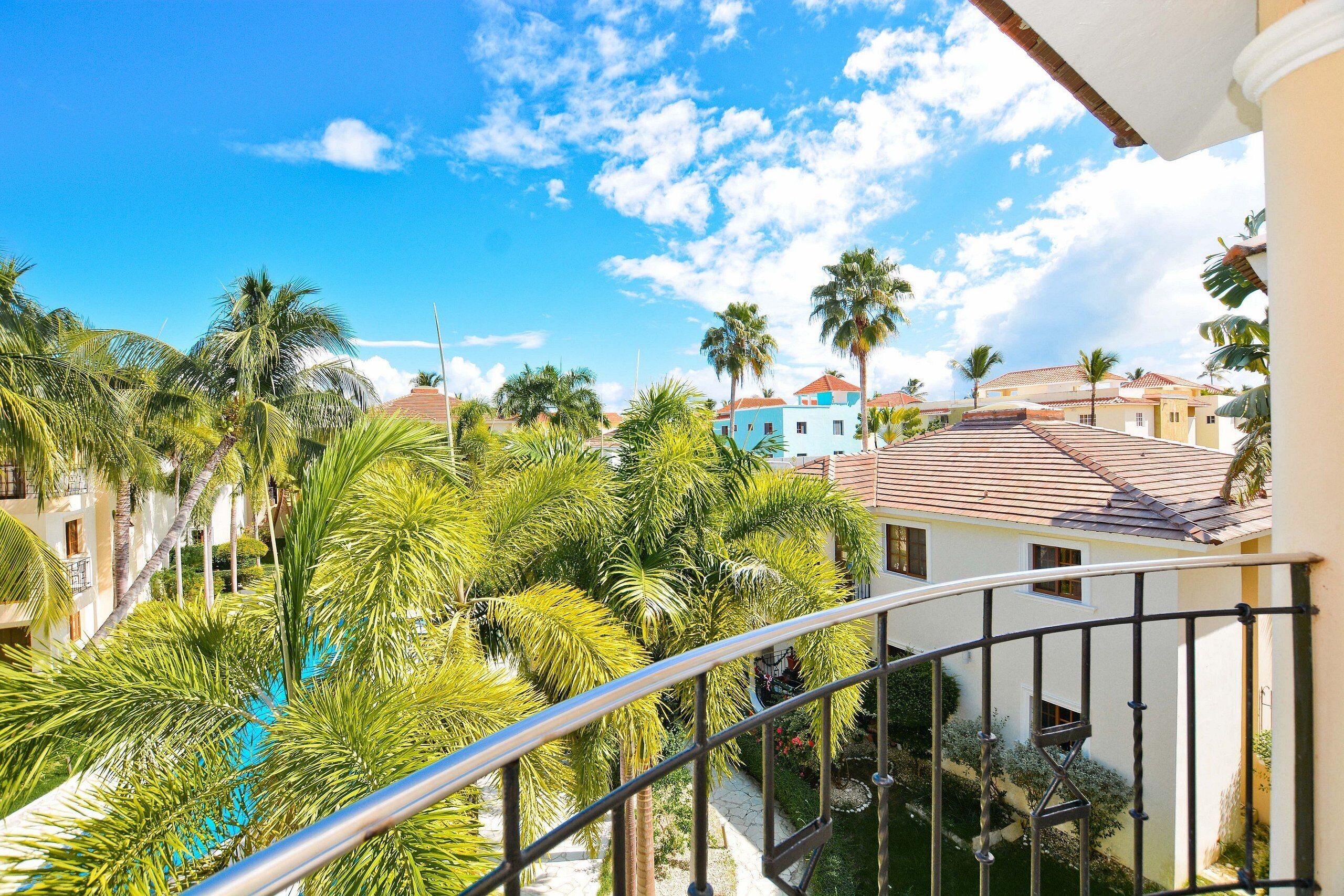 A balcony with a view of a swimming pool surrounded by palm trees and buildings.