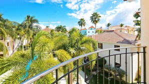 A balcony with a view of a swimming pool surrounded by palm trees and buildings. - Rosa Hermosa Penthouse | Pool View • Near Bávaro (Punta Cana)