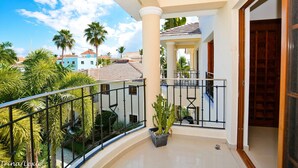 A balcony with a view of palm trees and a building in the background. - Rosa Hermosa Penthouse | Pool View • Near Bávaro (Punta Cana)