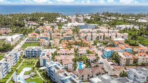 An aerial view of a resort with multiple buildings, a swimming pool, and a view of the ocean. - Rosa Hermosa Penthouse | Pool View • Near Bávaro (Punta Cana)