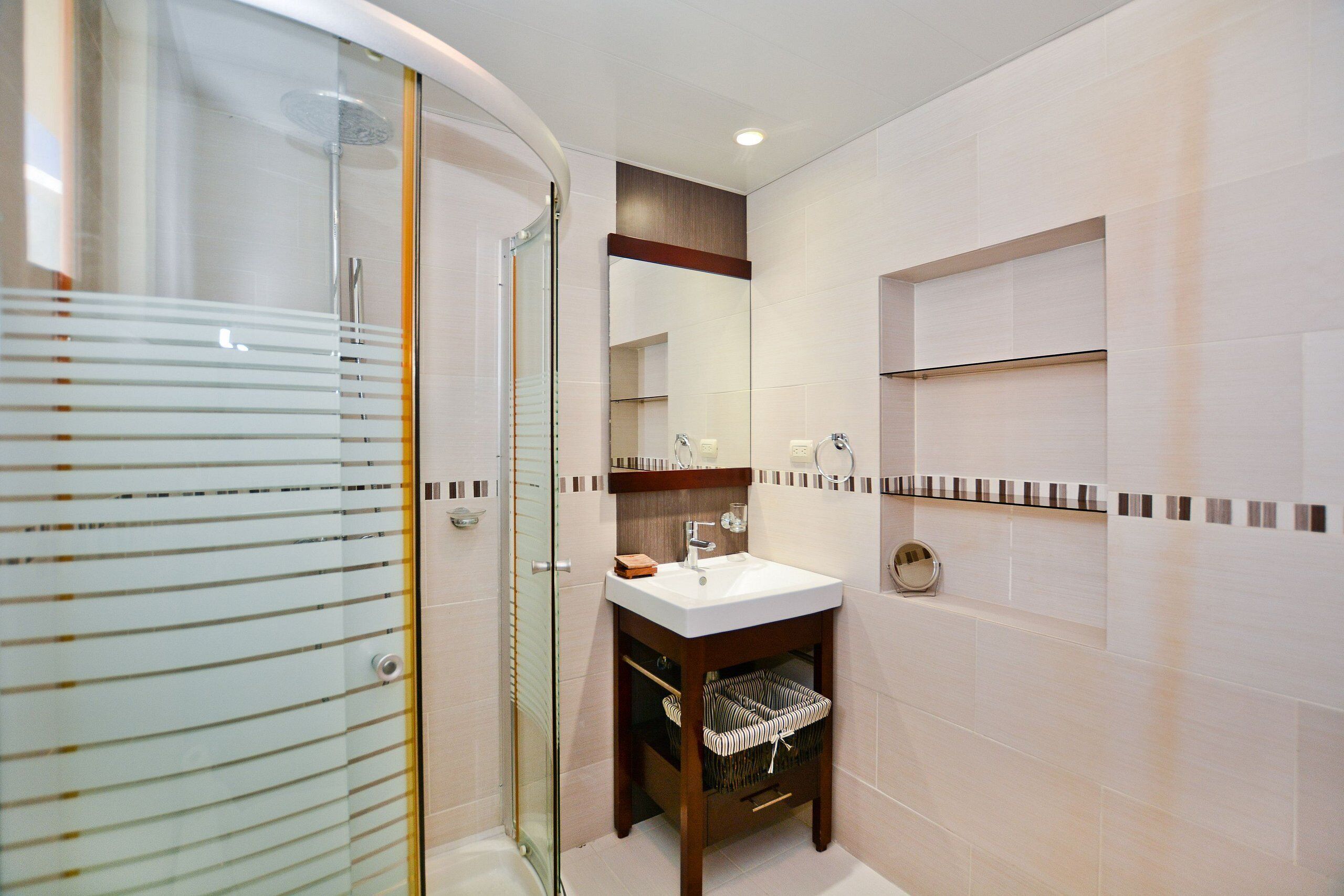 Un baño con cabina de ducha de vidrio, un lavabo blanco y un mueble de tocador de madera con espejo.