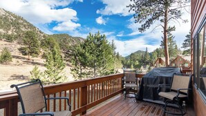 Terraza de madera con asientos exteriores, con vistas a un paisaje montañoso.