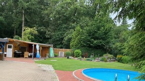 Een achtertuin met een zwembad, een barbecuehoek en een overdekt terras.