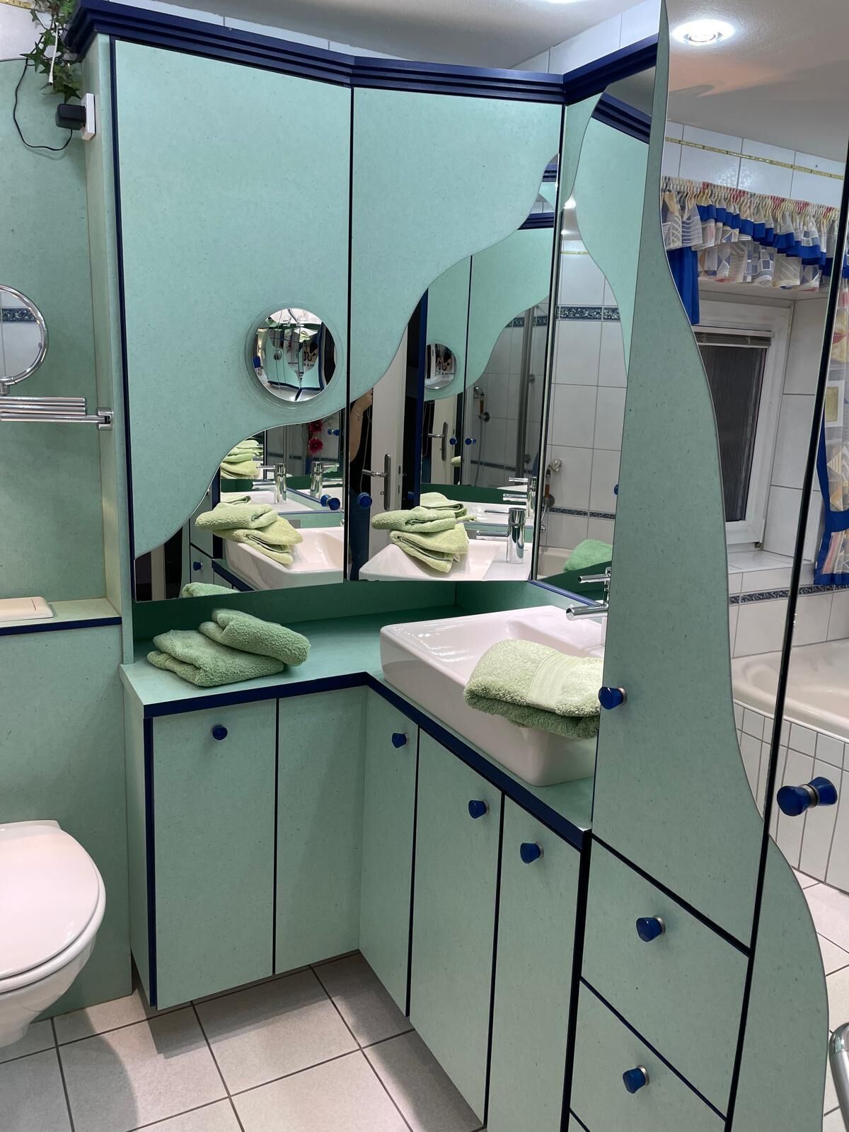 Une salle de bain avec un meuble-lavabo vert, un évier, un miroir et des toilettes.