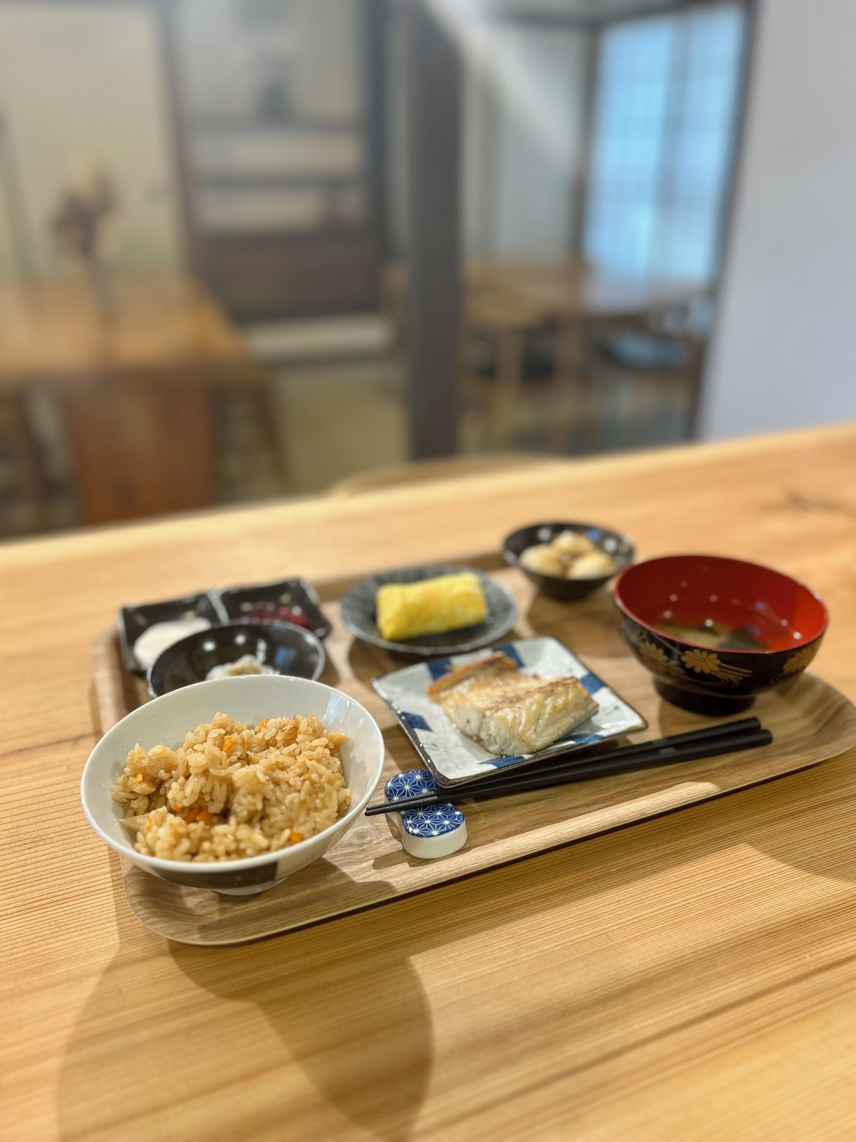 Taula de fusta amb un plat portar plats que conté diversos menjars, incloent arròs, peix i un bol de sopa.