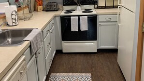 Una cocina con armarios blancos, estufa, microondas, refrigerador y una alfombra estampada.