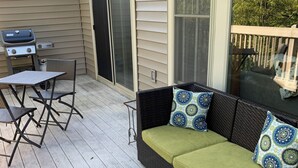 Un patio al aire libre con un sofá de mimbre, cojines verdes, una mesa de metal y sillas.