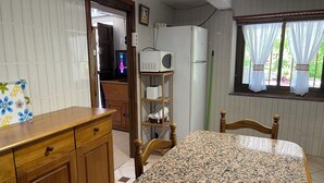 A kitchen with a granite countertop, wooden cabinets, a microwave, a refrigerator, and a window with curtains. - El Pedrosu (Infiesto)