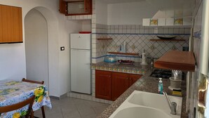 Een kleine keuken met een koelkast, houten keukenkastjes, een betegelde achterwand en een spoelbak.