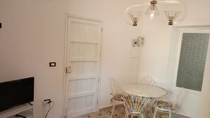Een kamer met een witte deur, een televisie op een standaard, een ronde tafel met stoelen en een kamer met een patroon vloer.