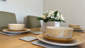 Ein Esstisch mit einer weißen und golden verzierten Tasse und Untertasse, einer Vase mit weißen Blumen und einem grünen Stuhl.