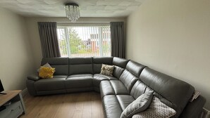 Ein modernes Wohnzimmer mit einer großen, ledernen L-Form-Couch, einem Holztisch und einer Pendelleuchte.