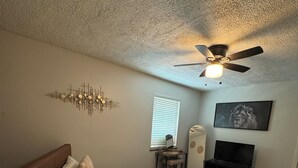 Une chambre à coucher comprenant un lit, un ventilateur de plafond, des œuvres d’art murales et un téléviseur.