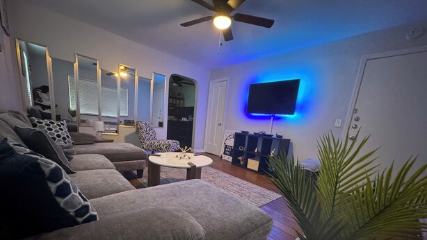 Un salon moderne avec un canapé, une table basse, un téléviseur fixé au mur et un ventilateur de plafond.