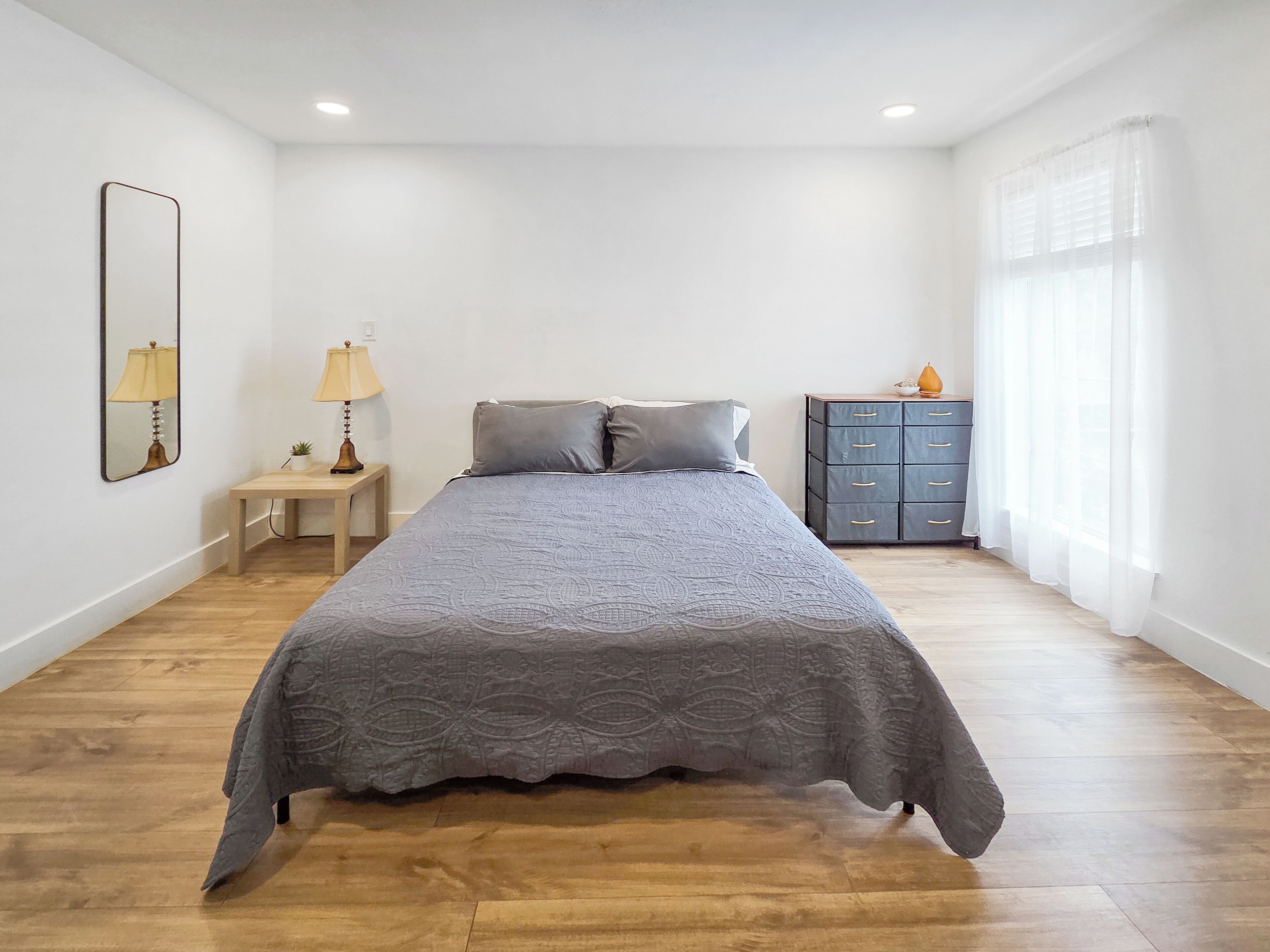 Een slaapkamer met een bed, nachtkastjes, een dressoir en een spiegel.