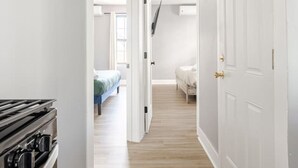 Ein Flur mit einer Küchenzeile links, einem Schlafzimmer mit Bett und Kommode in der Mitte und einem Badezimmer mit Toilette und Waschbecken rechts.