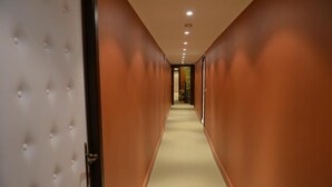Un pasillo con alfombra color crema, paredes de madera y una puerta capitonada a la izquierda.