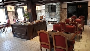Un restaurante con chimenea de piedra, sillas tapizadas en rojo y una zona de bar con mostrador de madera.
