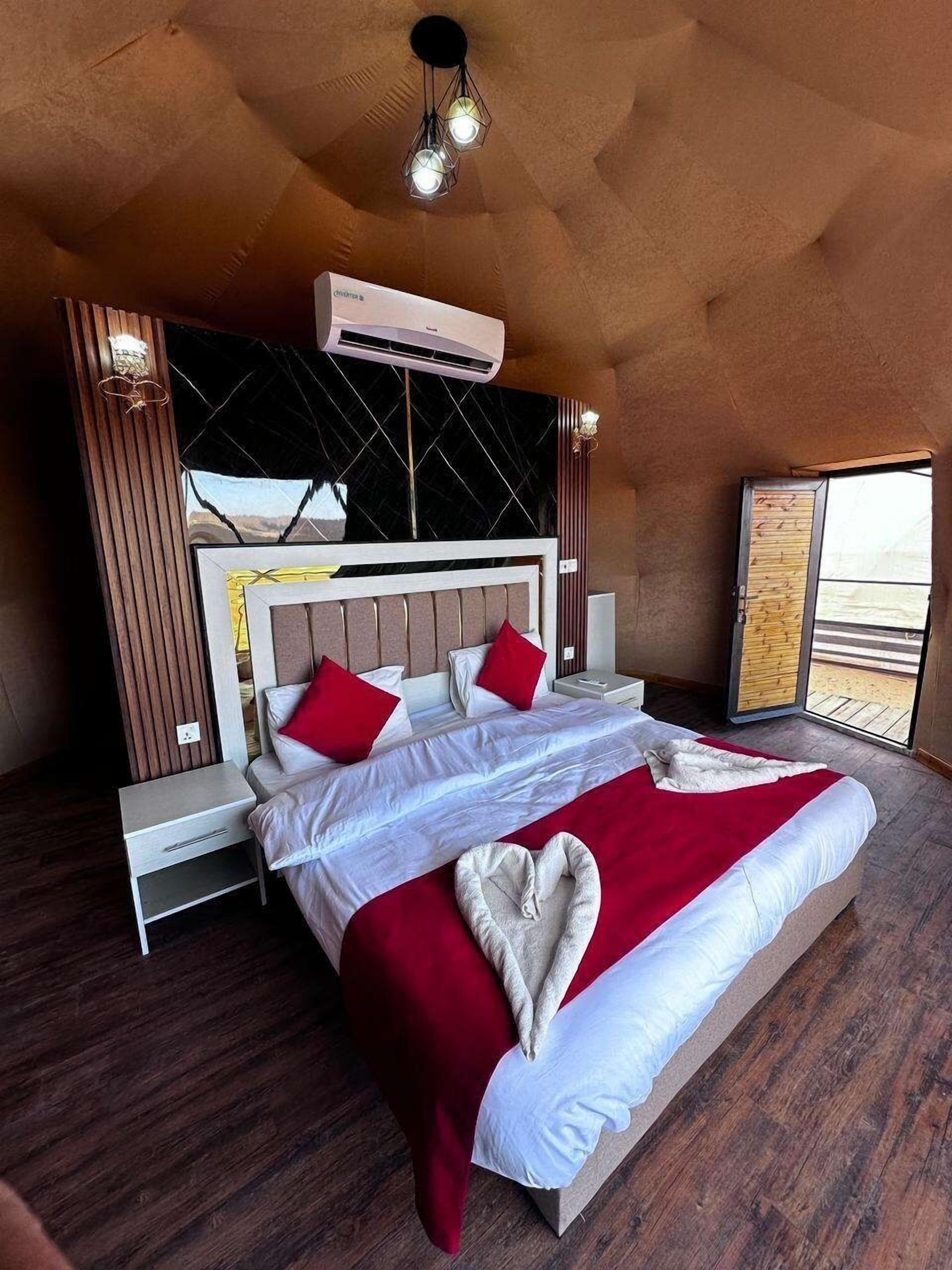 A bedroom with a bed, bedside tables, an air conditioning unit, and a view of the outdoors.