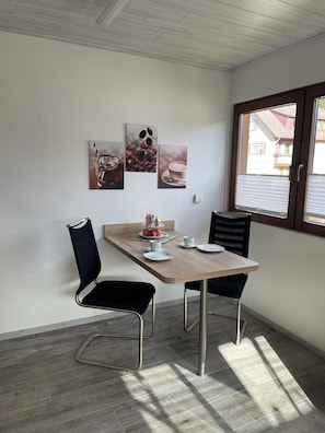 A dining area with a wooden table, two black chairs, and three coffee-themed wall art pieces.