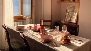 A dining table set with pink plates, glasses, and a bottle of wine, with a view of the sea through a window. - Casa Oliva Castelletto sul Garda - Natura Pura in Vista Lago (Brenzone sul Garda)