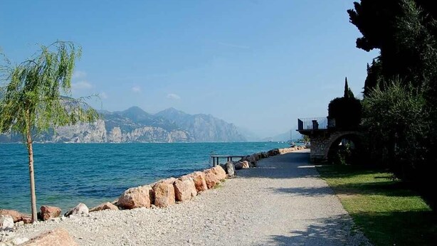 A coastal path with a rocky shoreline, a small bridge, and a gazebo-like structure. - Casa Oliva Castelletto sul Garda - Natura Pura in Vista Lago (Brenzone sul Garda)