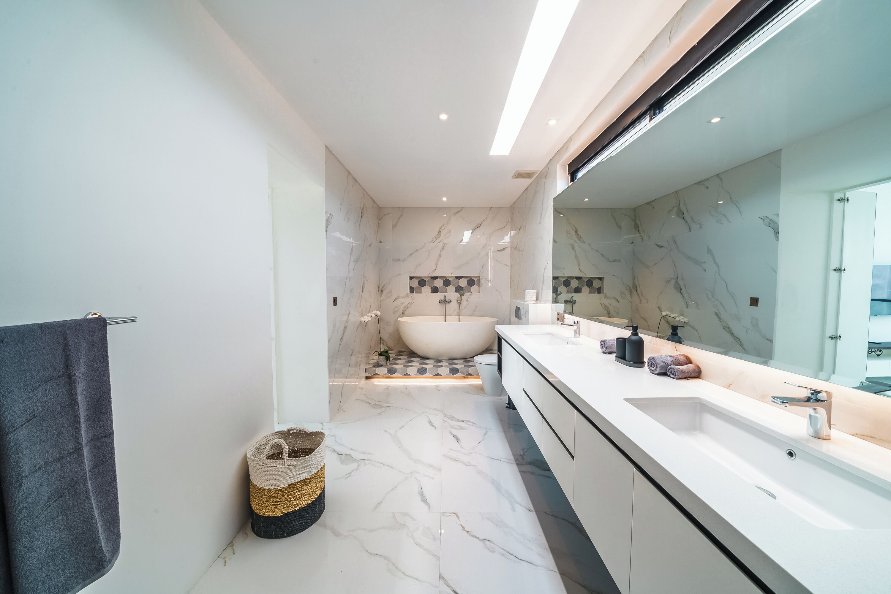 A modern bathroom with a large mirror, a bathtub, and a white vanity.