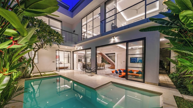 A modern house with a glass-enclosed pool, a staircase, and a dining area. - Villa Blue Water by GORO (Seminyak)