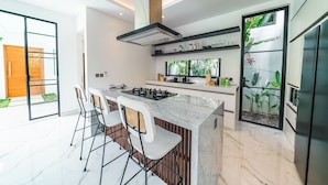 A modern kitchen with a central island, bar stools, and a built-in stove. - Villa Blue Water by GORO (Seminyak)