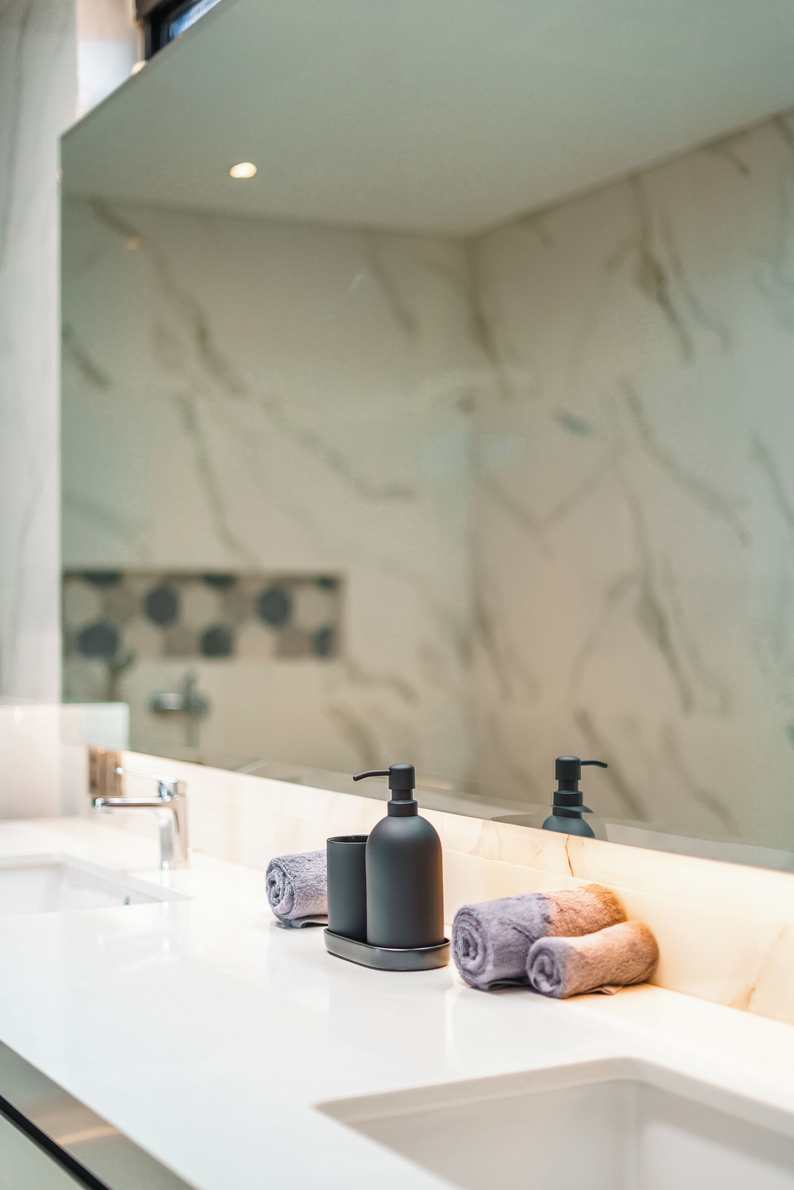 A bathroom with a white sink, black soap dispensers, and rolled towels on the counter.