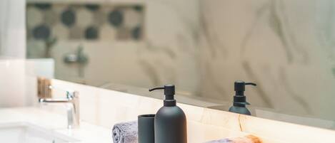 A bathroom with a white sink, black soap dispensers, and rolled towels on the counter.