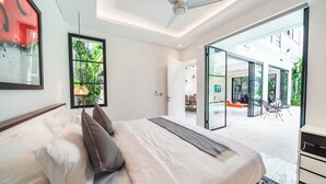 A modern bedroom with a large bed, a ceiling fan, and a view of an outdoor patio area. - Villa Blue Water by GORO (Seminyak)