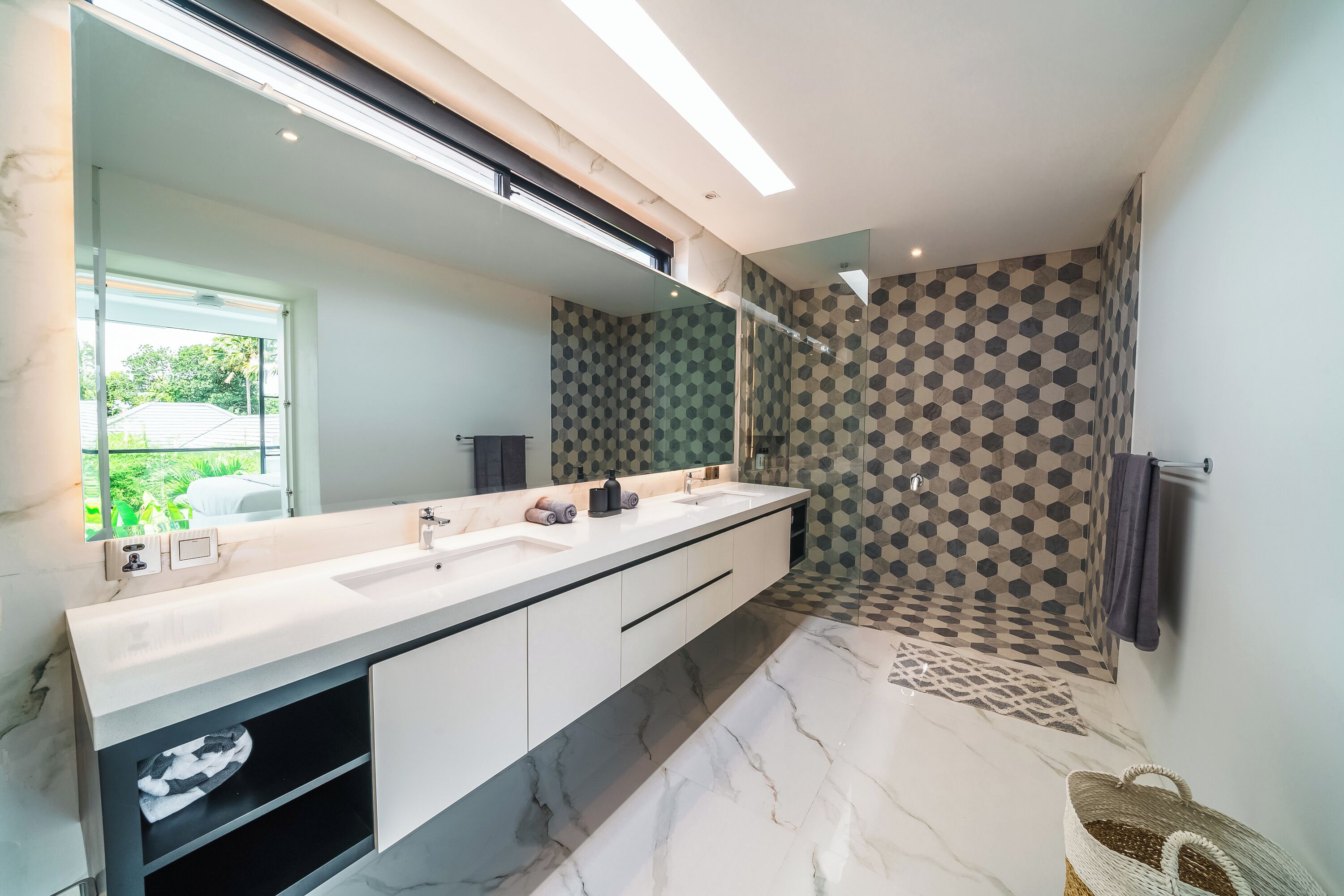 A modern bathroom with a large mirror, two sinks, a shower area, and a patterned floor.