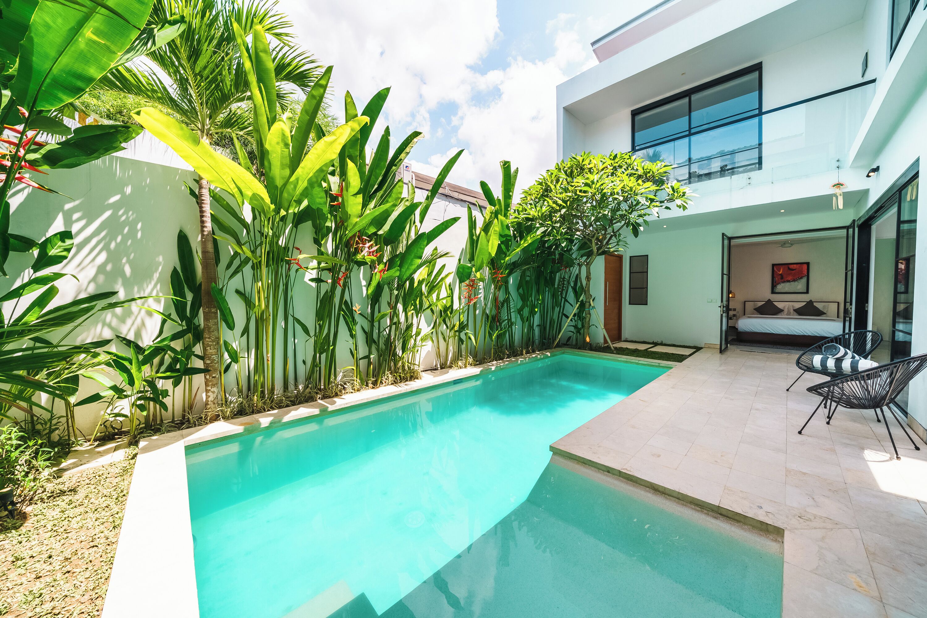 A modern house with a swimming pool, surrounded by lush greenery and a patio with outdoor furniture.