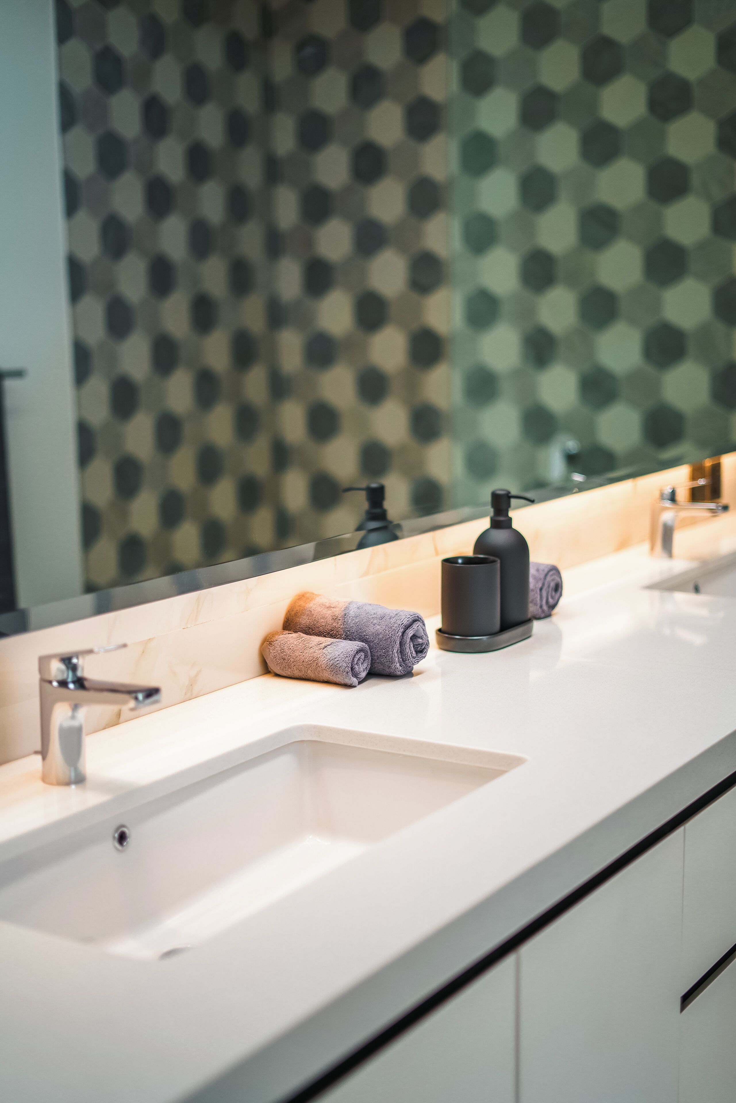 A modern bathroom with a white sink, two faucets, and a large mirror.