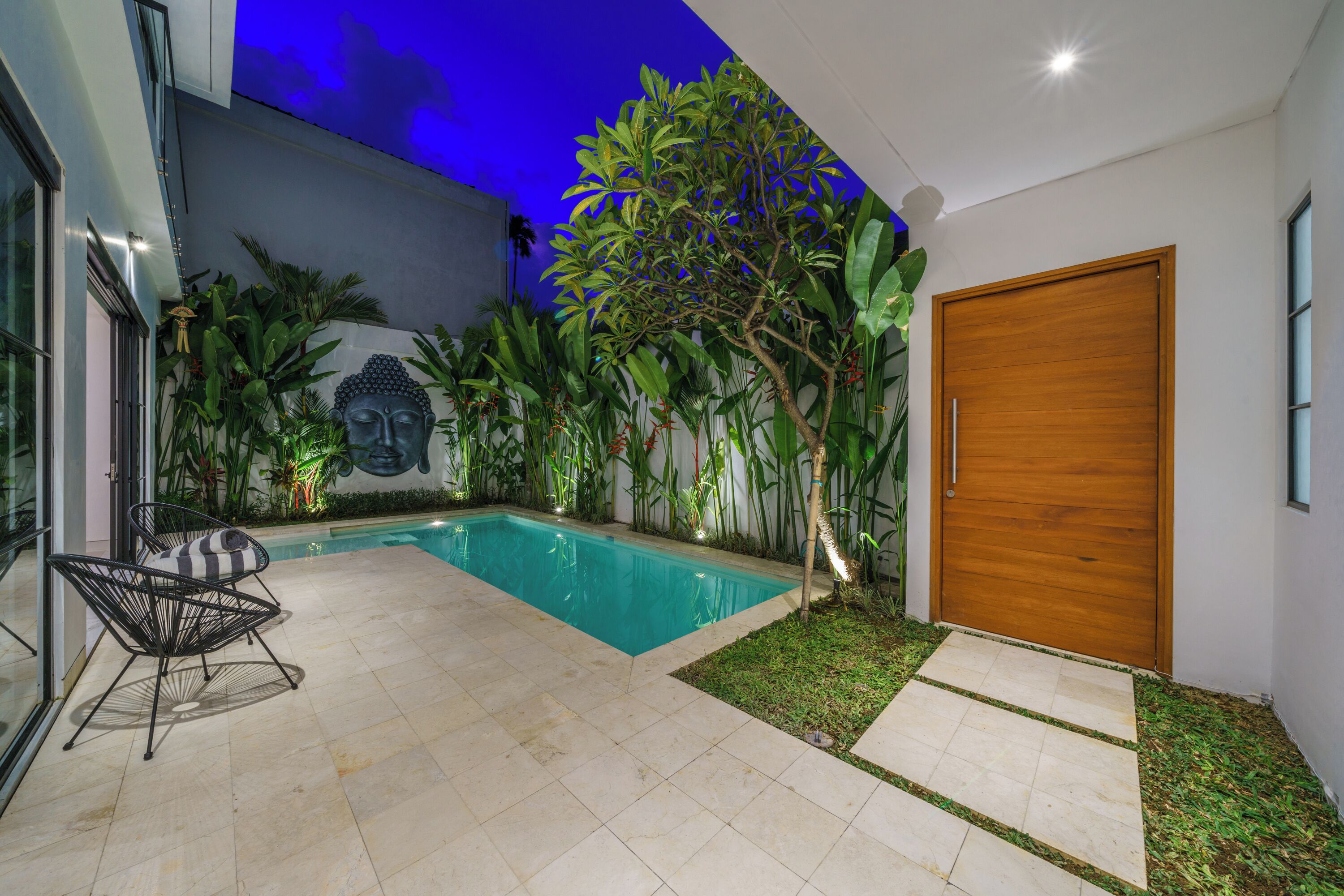 A modern outdoor pool area with a wooden door, a chair, and various plants.