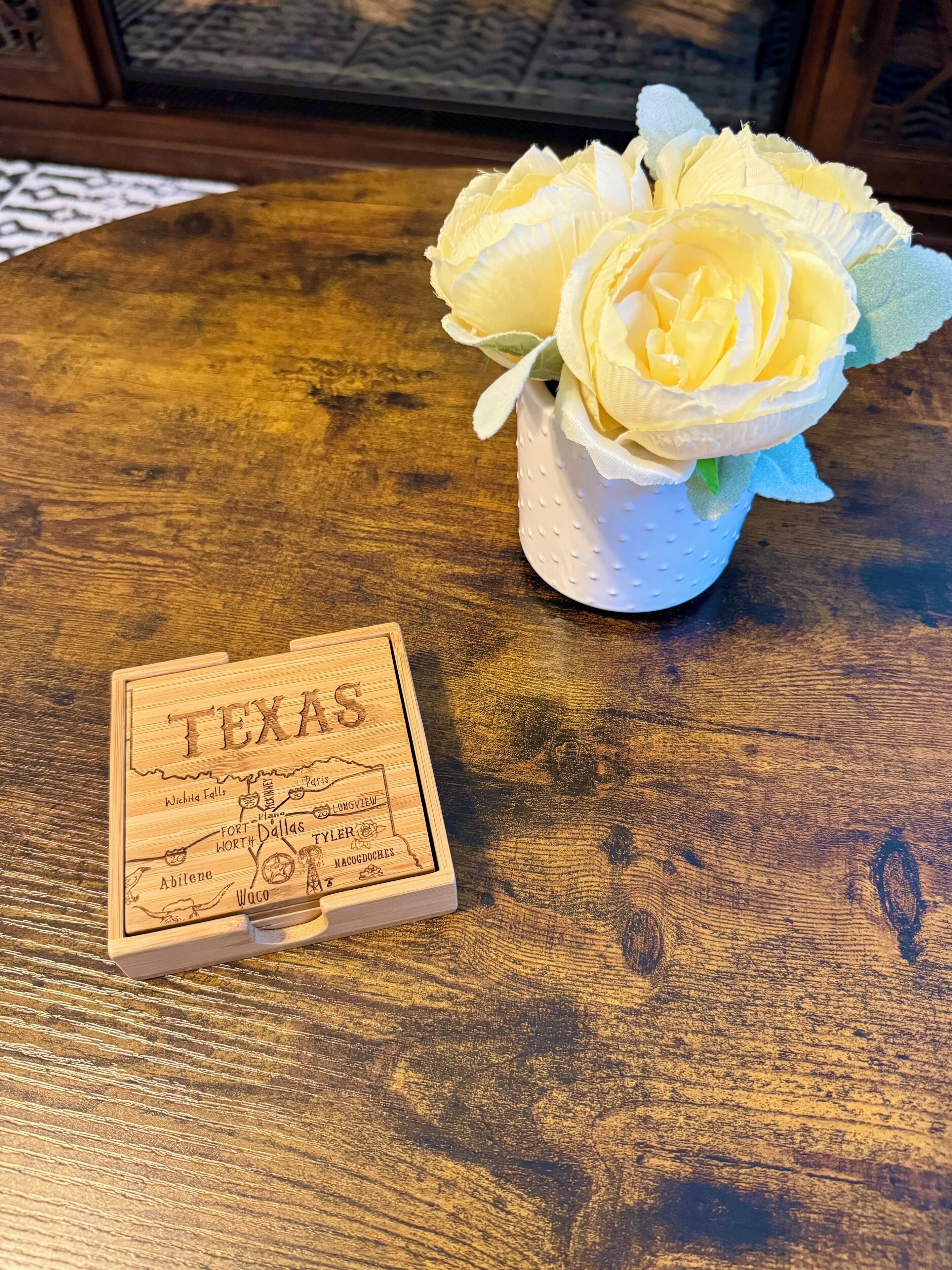 A wooden table with a white vase containing yellow flowers and a wooden box labeled "TEXAS" with landmarks.