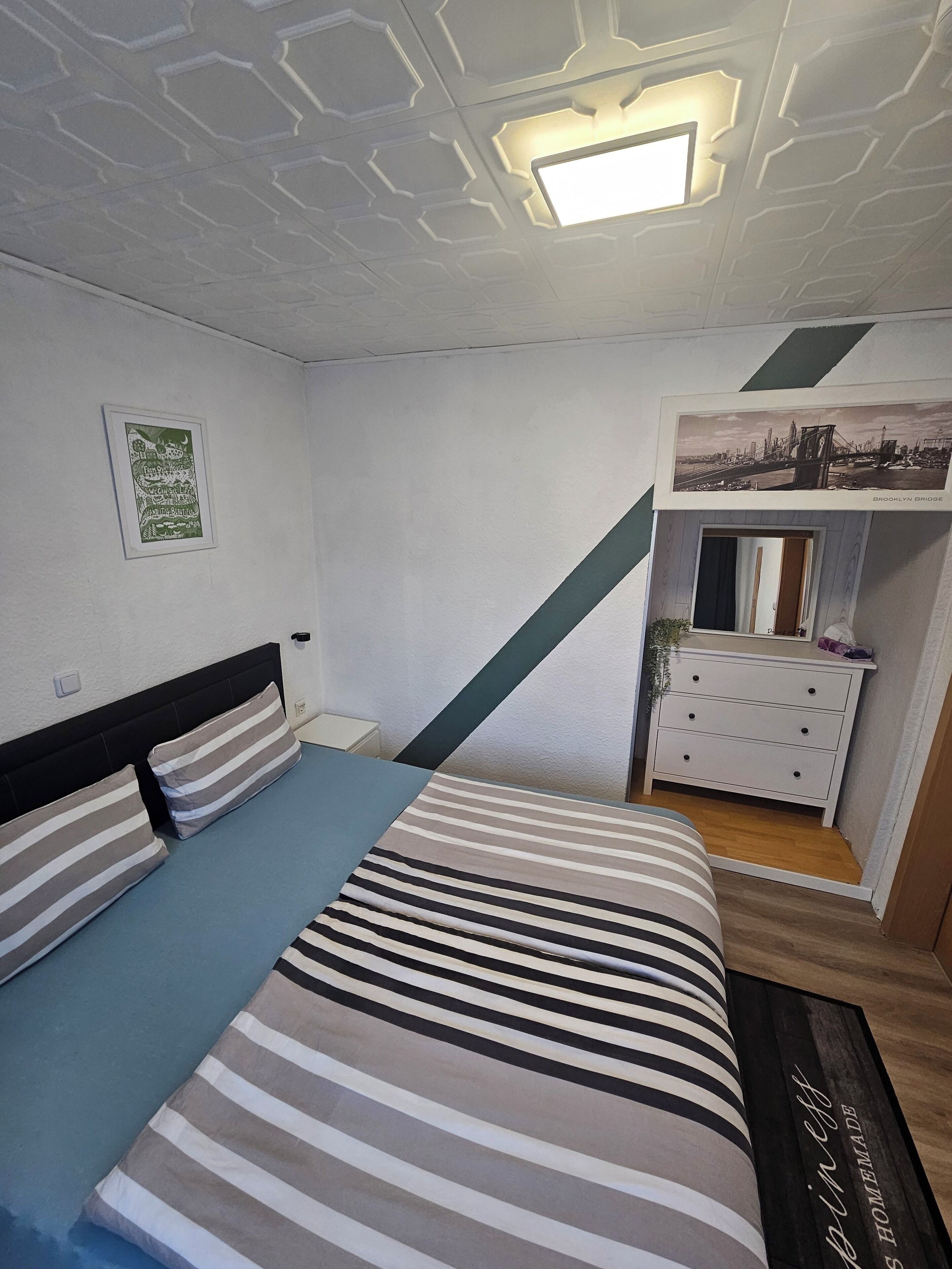 A bedroom with a bed, a dresser, a framed picture, and a ceiling light.