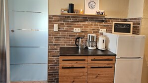 Een keuken met een bakstenen muur, houten kasten, een Bosch koelkast, een koffiezetapparaat en een prikbord waarop 'Danke' staat.