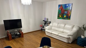 Un salon moderne avec un canapé en cuir blanc, un téléviseur à écran plat, une table basse en verre et un tableau accroché au mur.